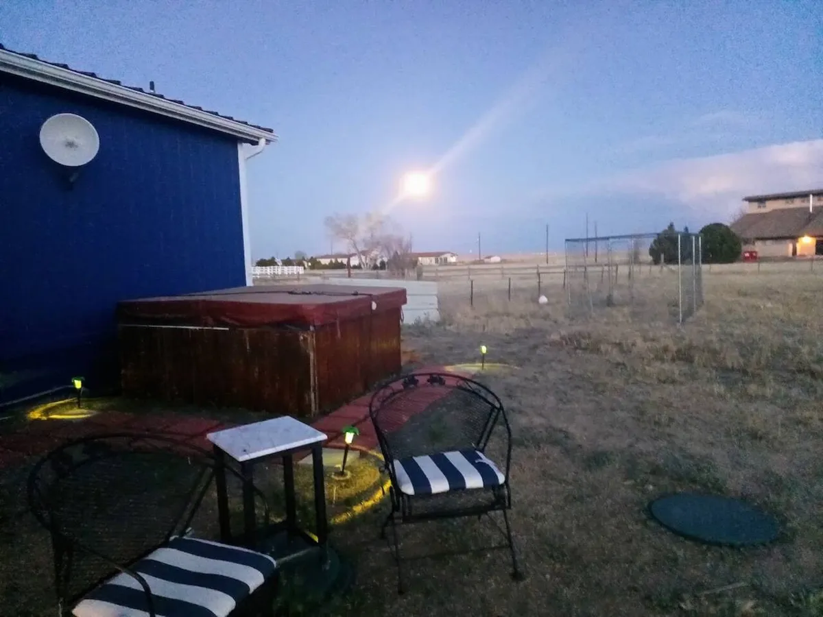 This image features a hot tub with a comfortable seating area and the moon visible above, suggesting a tranquil evening setting. The patio is set up for relaxation and social gatherings under the open night sky, perfectly capturing the ambiance of soaking in a private hot tub while stargazing.