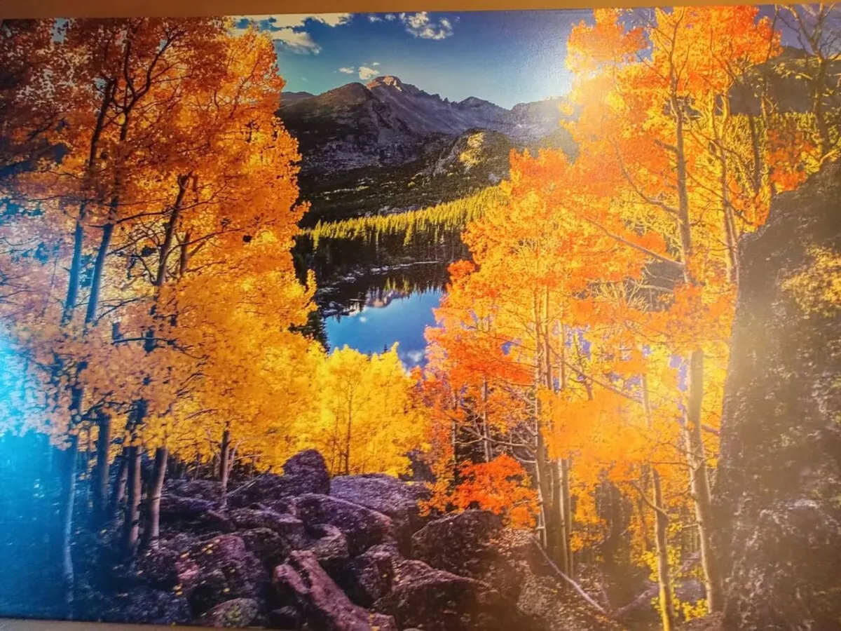 This image captures brightly colored autumn trees reflected in a tranquil lake with distant mountains in the background and a rocky foreground. The overall scene is vibrant, peaceful, and perfectly illustrates a serene mountain setting ideal for quiet moments and nature appreciation.