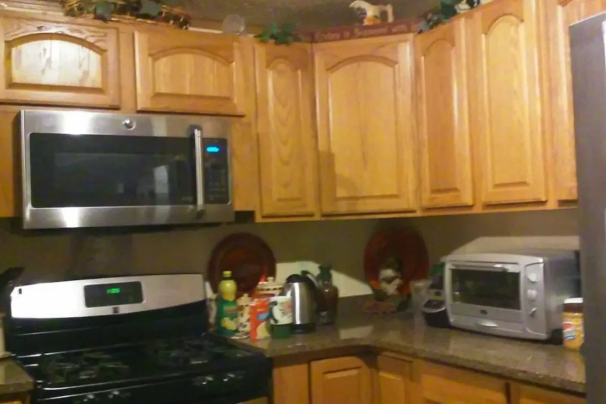A welcoming kitchen scene featuring wooden cabinets, stainless steel appliances, and countertop decorations. The space looks ready for meal preparation, baking, and family gatherings, with ample room for multiple people to cook together.